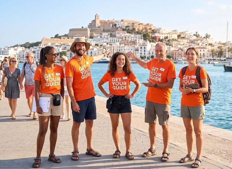A group of people wearing orange shirts with 'GET YOUR GUIDE' text, standing on a waterfront promenade with a historic cityscape in the background. 2