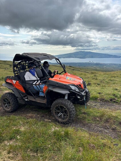 A person riding a red and black ATV on a grassy hill with a lake and mountains in the background. 2
