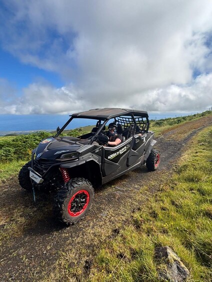 A black ATV with red rims on a dirt path with grass on either side. 1