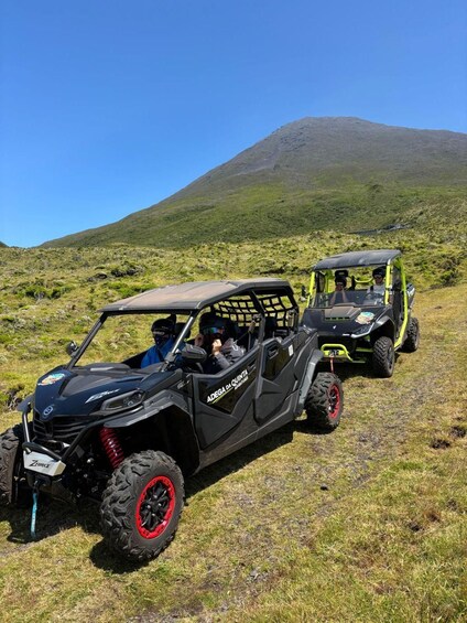 Two off-road vehicles on a grassy hillside with a mountain in the background. 4