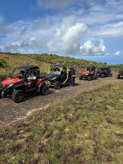 Off-road vehicles parked on a grassy field with a hilly landscape in the background. 5