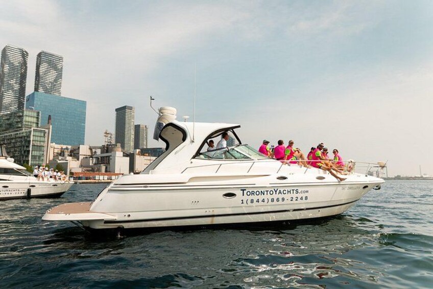 A white yacht with people on board, a city skyline in the background, and the text 'TorontoYachts.com' on the side. 1