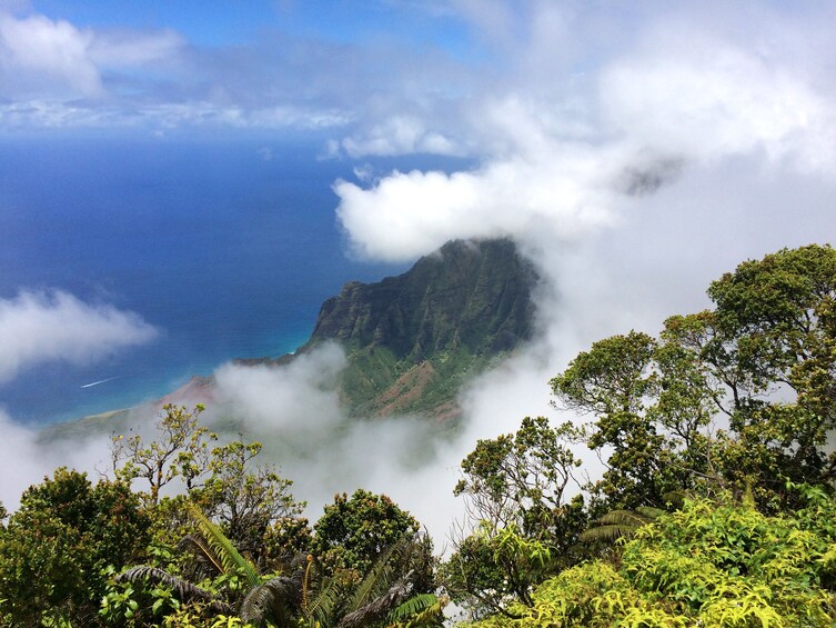 A mountainous landscape with lush greenery, a clear blue sky, and a view of the ocean. 1
