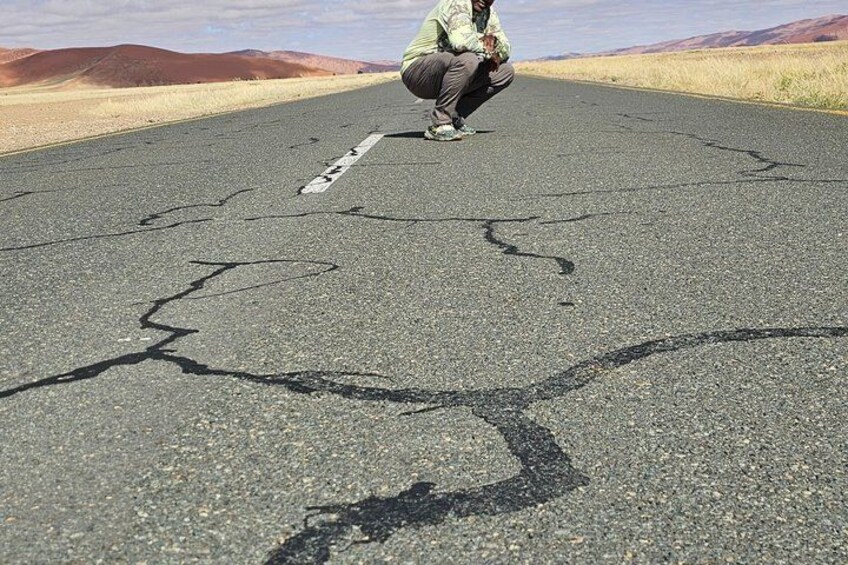 A person crouching on a cracked road with a mountainous landscape in the background. 2
