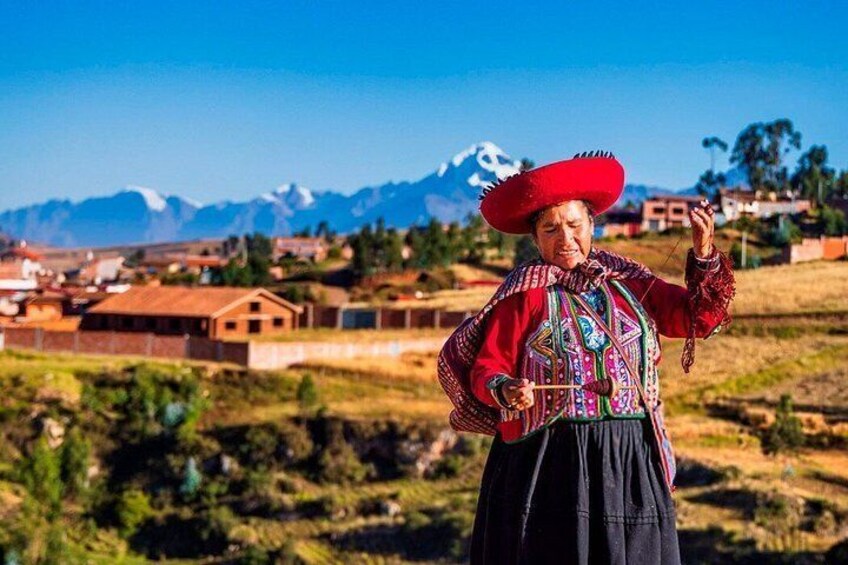 A person in traditional attire with a red hat, standing in a rural landscape with houses and mountains in the background. 5