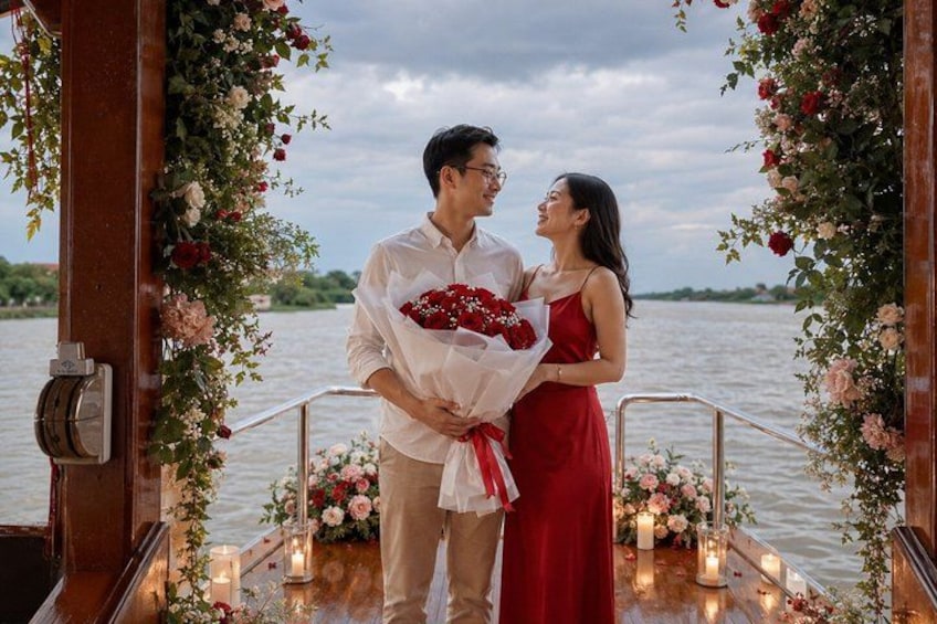 A couple standing on a boat deck with a floral arch and candles. 1