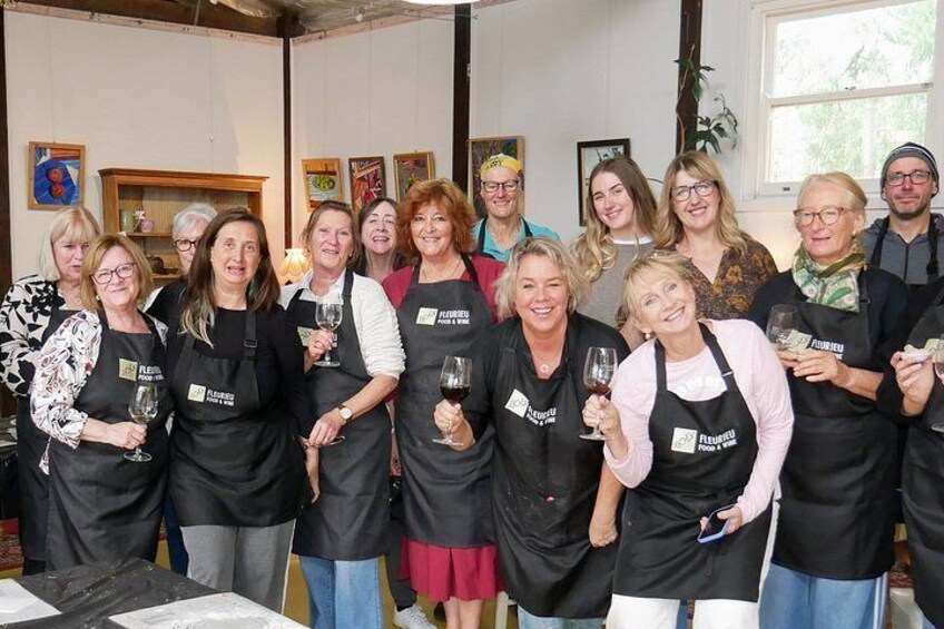 A group of people wearing aprons with the logo 'Flavors Food & Wine' in a room with paintings on the walls. 2