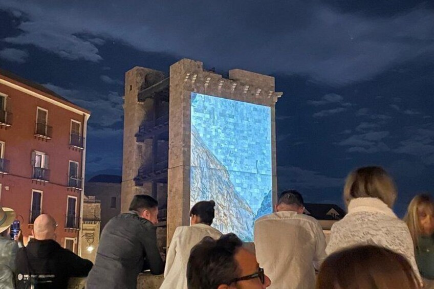 A crowd gathered around a digital display on a building, with a cityscape in the background. 4