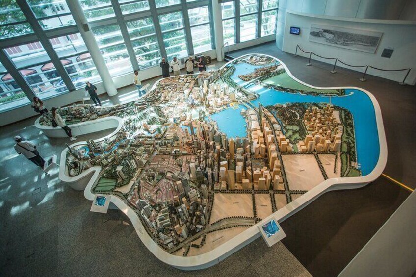 A detailed scale model of a city with a central water feature, surrounded by various buildings and greenery. 2