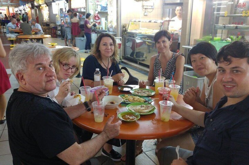 A group of people sitting around a table with food and drinks in a busy indoor setting. 1