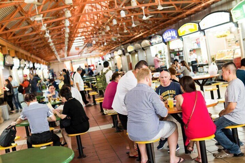 A bustling indoor market with people seated at tables, various food stalls, and a high ceiling with exposed beams. 4