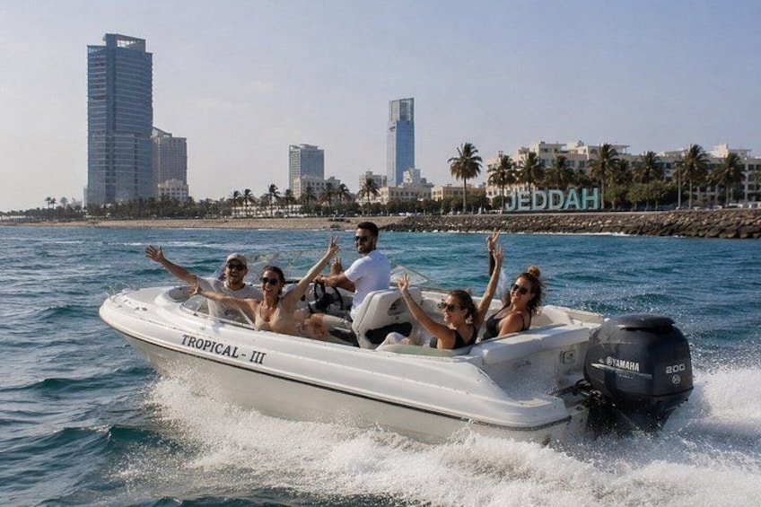 Een boot genaamd 'TROPICAL - III' op het water, met een stadsachtergrond op de achtergrond. 1