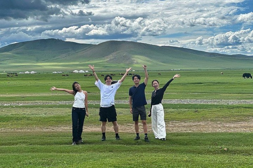 Four people standing in a grassy field with mountains in the background. 4