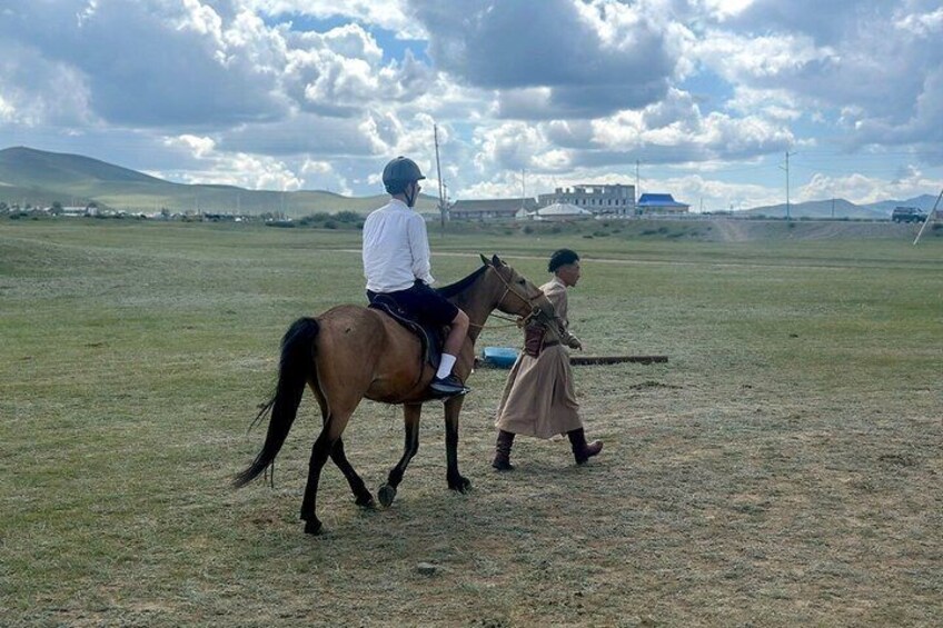 A person riding a horse in a grassy field with a building in the background. 2