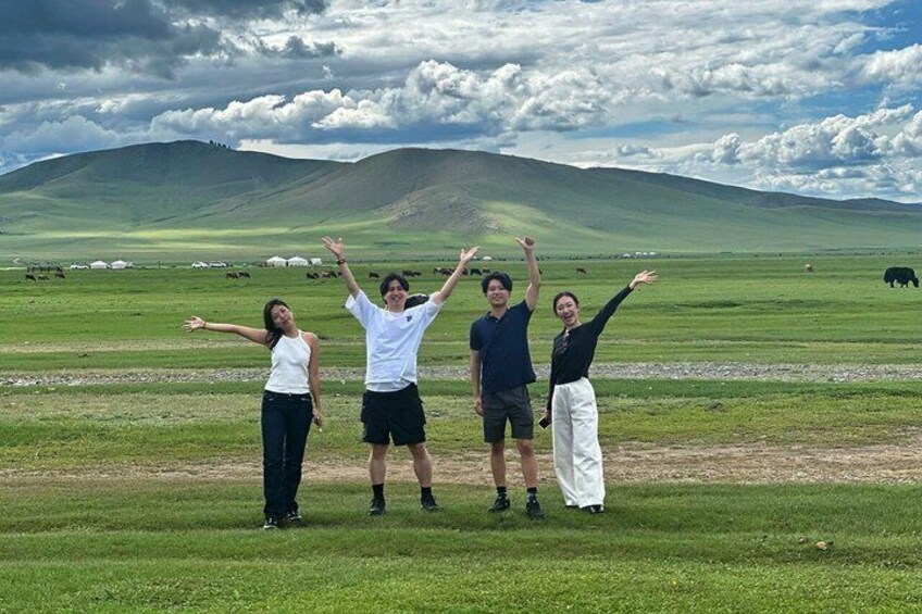 A group of people standing in a grassy field with mountains in the background. 4