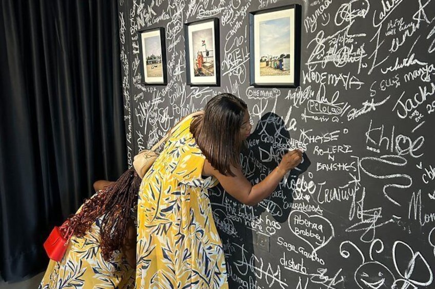 A person writing on a wall with various signatures and drawings. 1