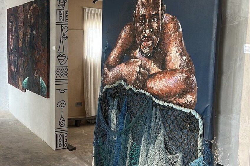 A room with a large painting of a person in a blue garment, a patterned wall, and a white curtain. 2