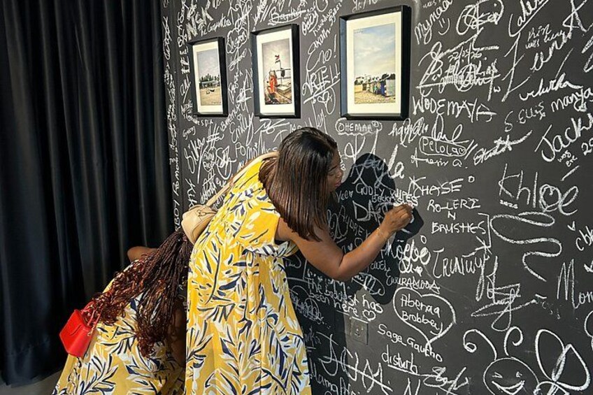 A person writing on a wall covered with various names and drawings. 1
