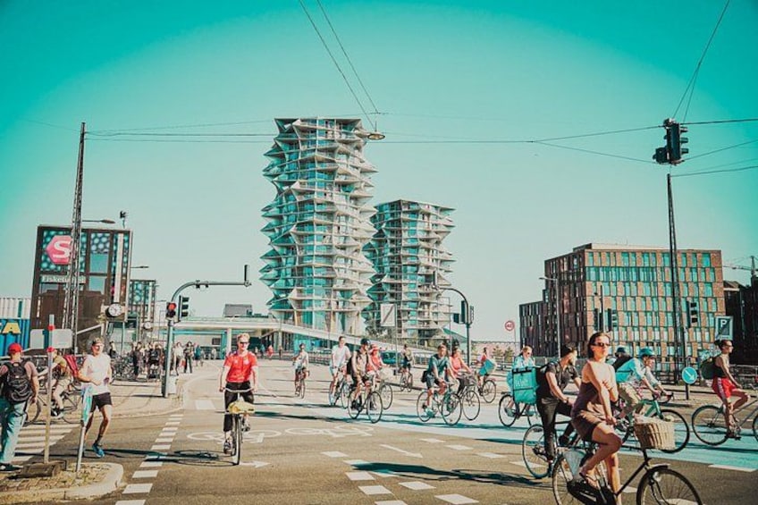 A busy street with cyclists, a modern building under construction, and a clear sky. 1
