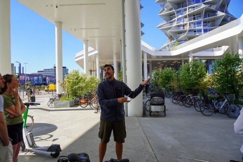 A person gesturing, a modern building, and bicycles in a public space. 3