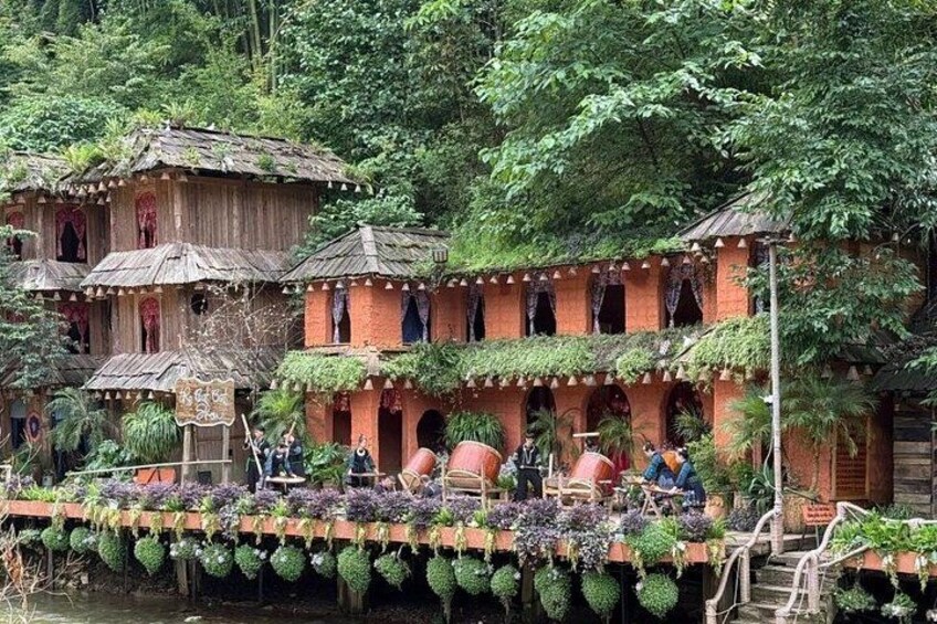 A traditional wooden house with a thatched roof, surrounded by lush greenery and a river. 3