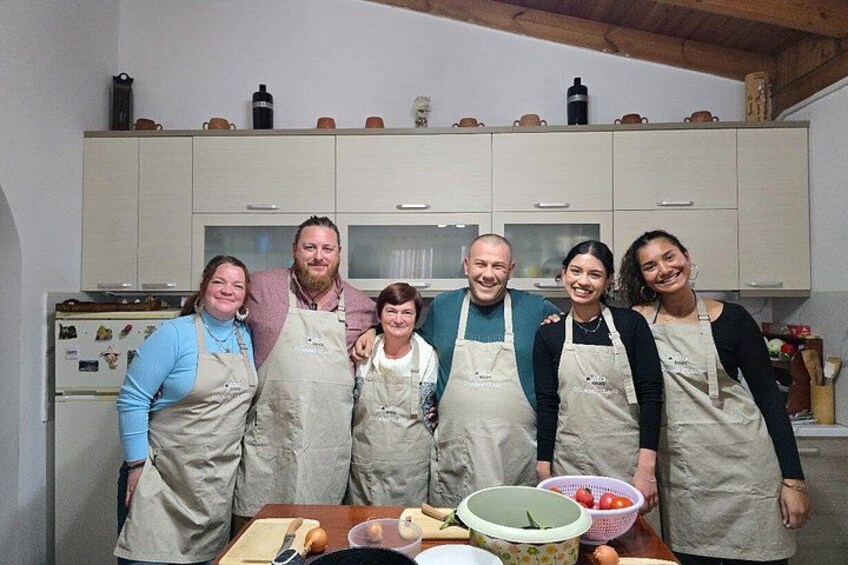 A group of people in a kitchen with cabinets and a table with food items. 1