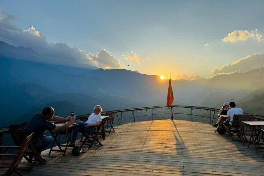 A sunset over a mountainous landscape with people sitting on a wooden deck. 4