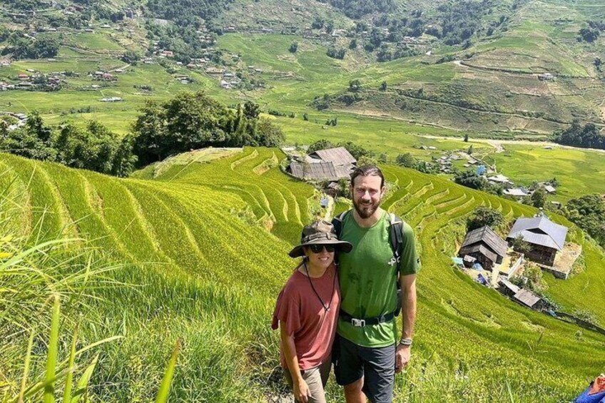 A person standing on a grassy hillside with terraced fields and traditional houses in the background. 5