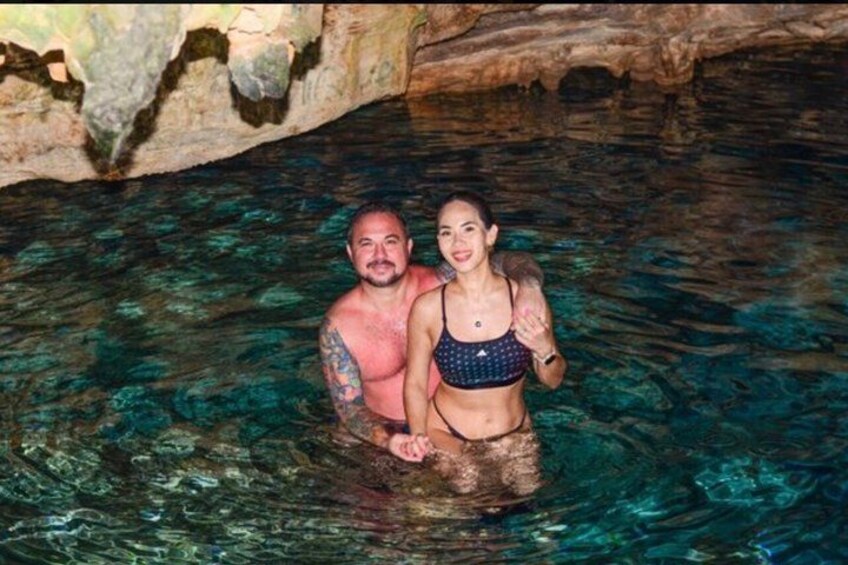Two people in a clear blue pool with rocky formations in the background. 4