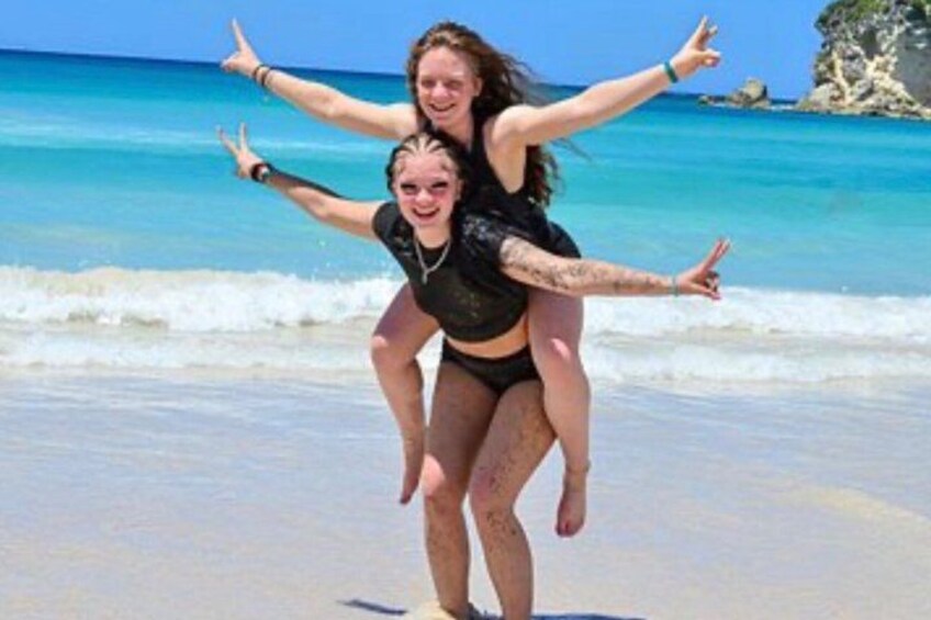 Two people on a beach with clear blue water and a rocky outcrop in the background. 3