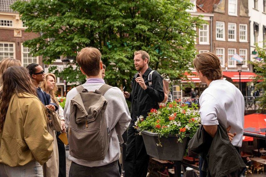 A group of people standing outdoors, some with backpacks, in an urban setting with buildings and a street vendor cart with flowers. 4