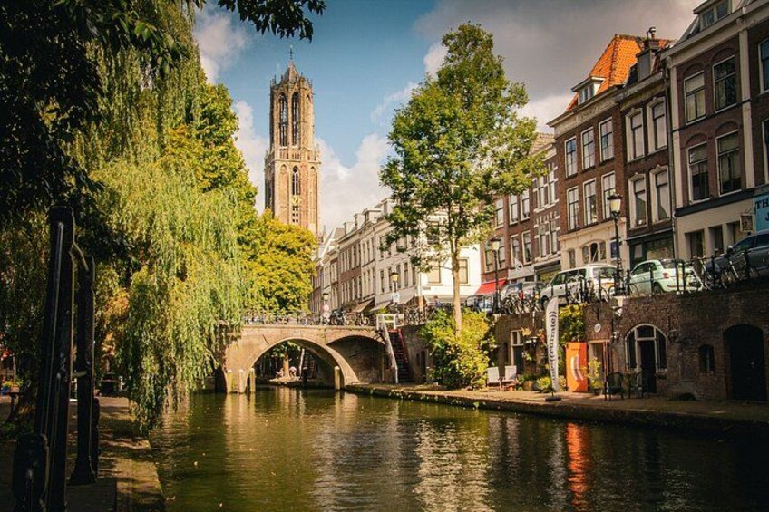 A canal with a stone bridge, historic buildings, and a tall church tower. 1