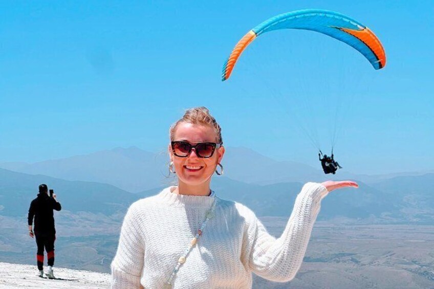 A person standing on a mountain with a paragliding activity in the background. 1