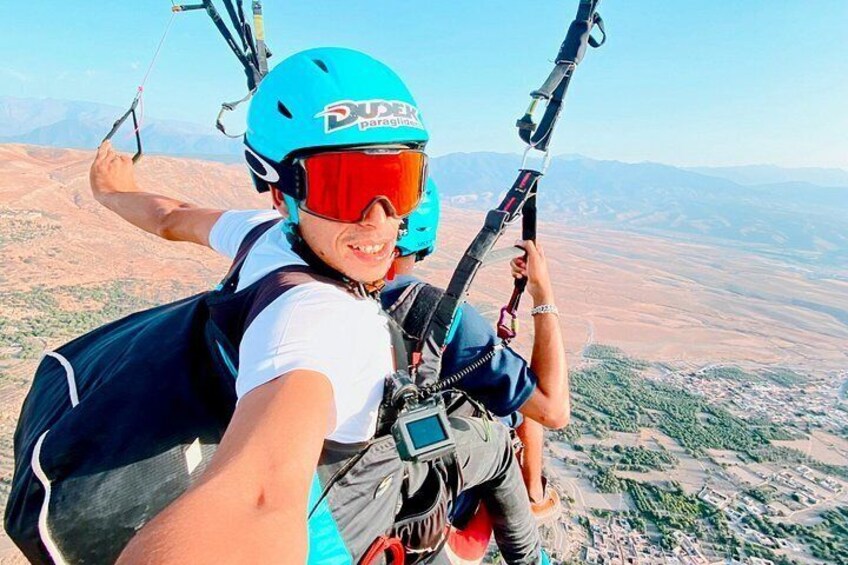 A person paragliding with a blue helmet and harness, over a mountainous landscape. 5