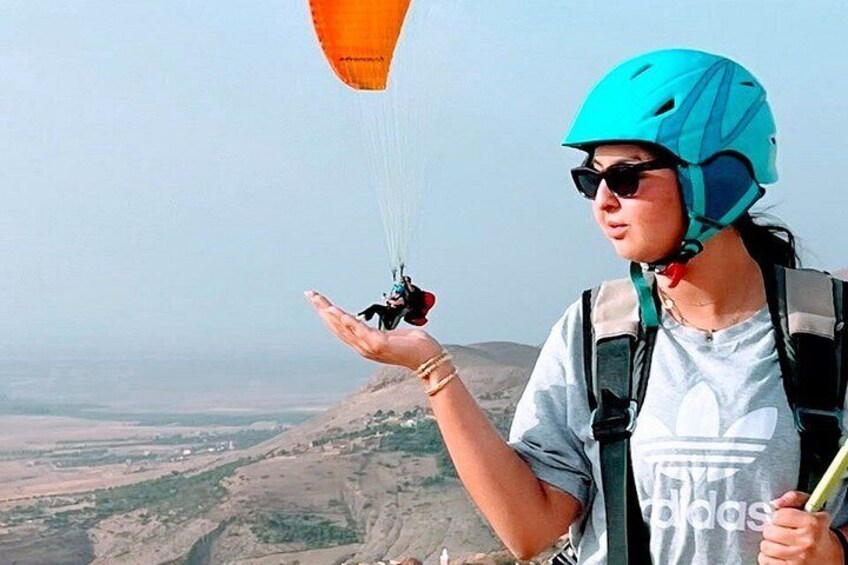 A person in a blue helmet and grey t-shirt holding a parachute, with a landscape in the background. 4