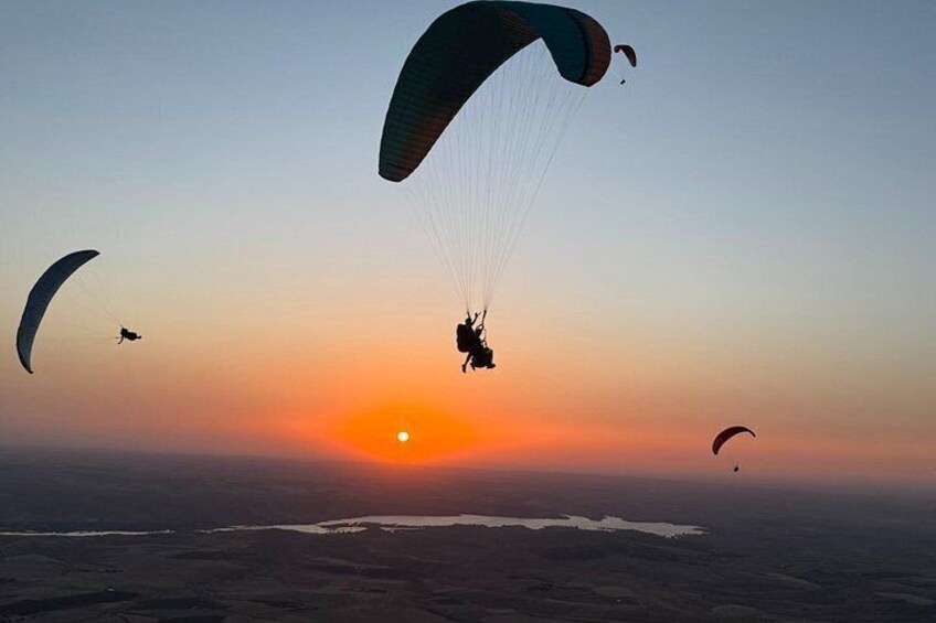 A person paragliding with a parachute above the ocean at sunset. 3
