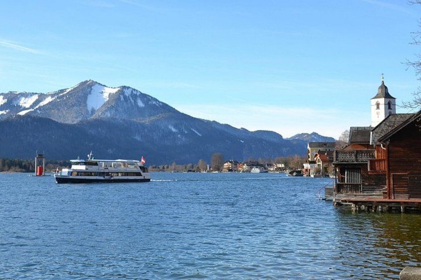 A boat on a lake with mountains in the background and a wooden building on the right. 1