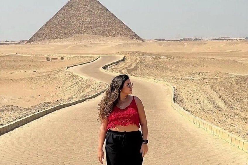 A person standing on a paved path with a pyramid in the background. 2