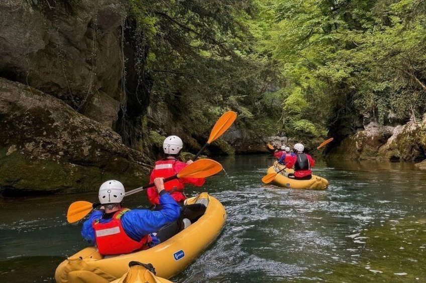 Three people kayaking on a river surrounded by rocky cliffs and dense greenery. 5