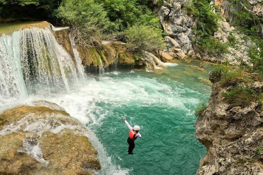 A person standing on a rock in a river with a waterfall in the background. 5