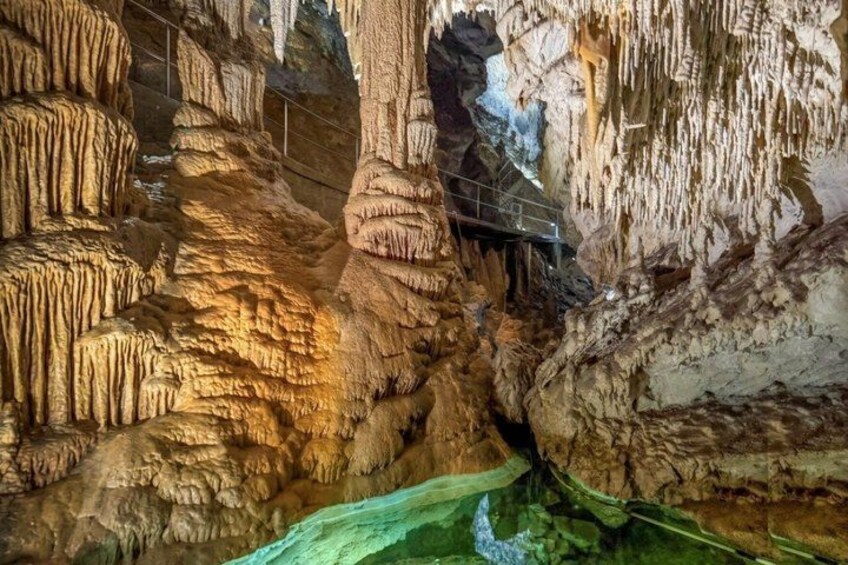 A cave with stalactites, a water stream, and a metal bridge. 1