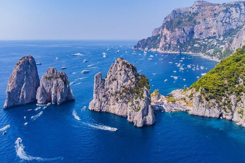A coastal landscape with rocky formations, clear blue sea, and boats. 1