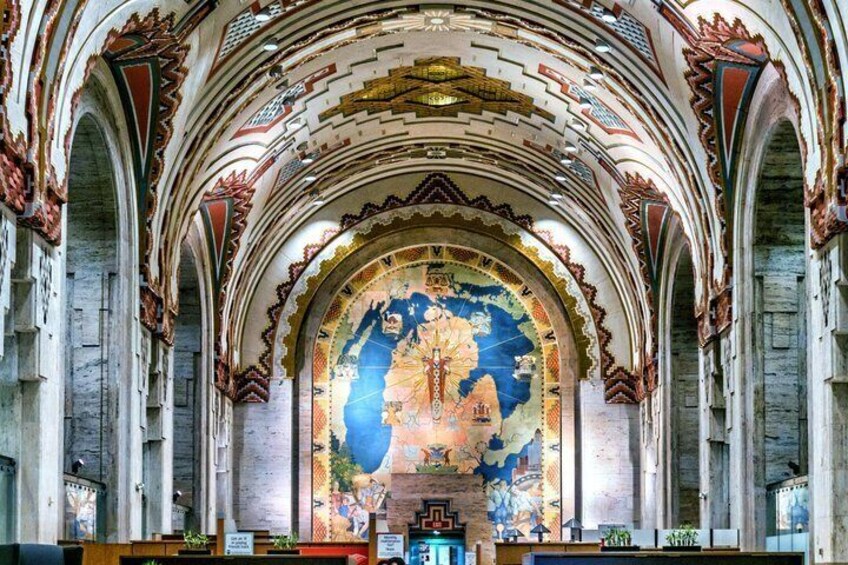 An interior with a large, colorful mural, arched ceilings, and stone columns. 1