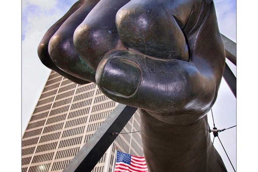 A close-up of a bronze statue of a clenched fist with an American flag in the background. 3