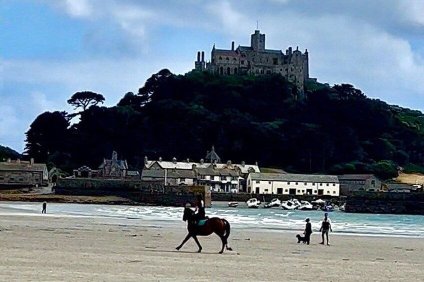 A beach with a castle on a hill, people walking, and a horse. 2