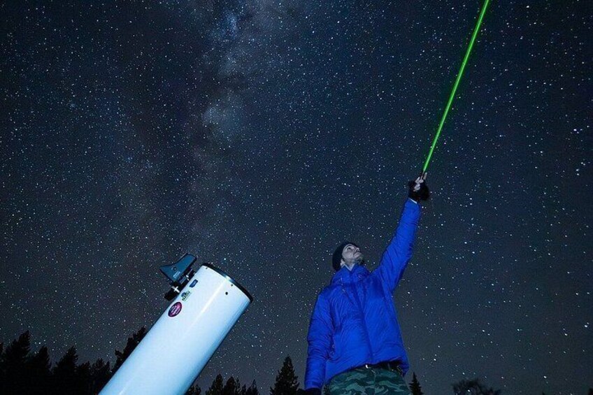 A person holding a green laser pointer against a starry night sky. 1