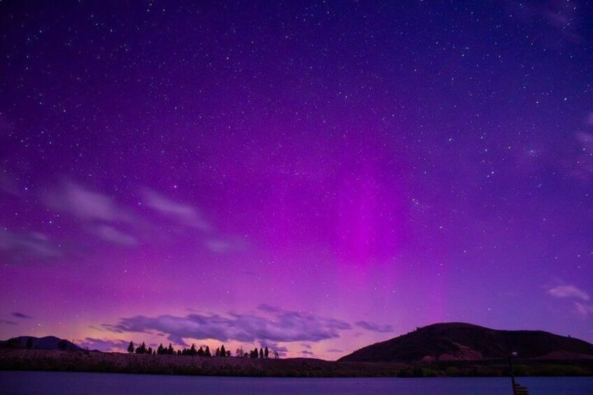 A night sky with stars and a purple aurora over a hilly landscape with a lake. 3