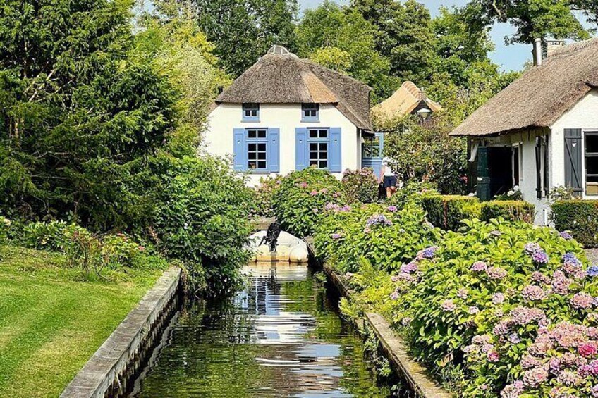 A narrow canal with houses on either side, surrounded by lush greenery and flowering plants. 2