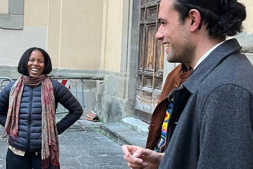 Two people standing on a street with a building in the background. 5