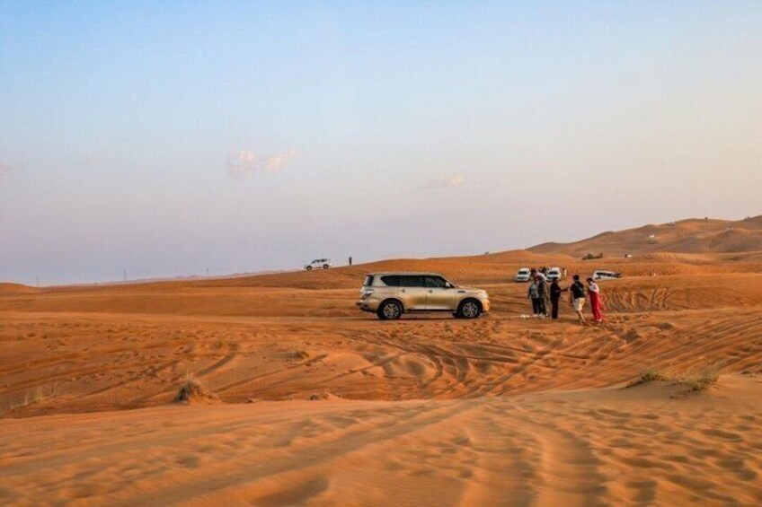 A desert landscape with sand dunes and a group of people standing near a vehicle. 3